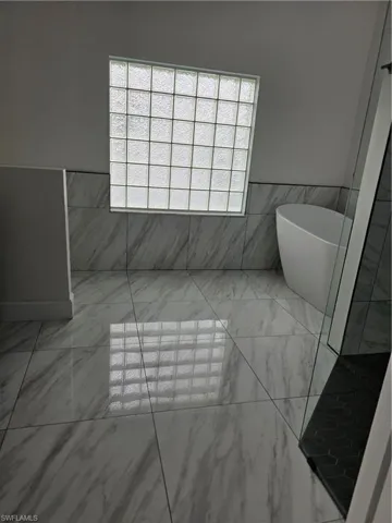 Full bathroom featuring a freestanding tub, a wainscoted wall, tile walls, and marble finish floors