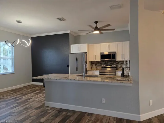 Kitchen with crown molding, appliances with stainless steel finishes, white cabinets, backsplash, and dark wood-style flooring