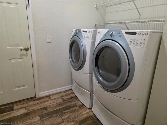 Washroom with a textured wall, washing machine and dryer, and dark wood-style flooring