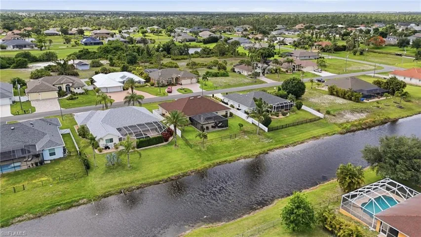 Waterfront property featuring a screened lanai, manicured lawn, and mature palm trees