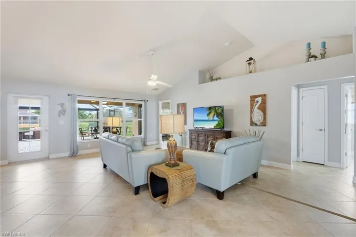 Spacious living area featuring vaulted ceilings, tile flooring, and large sliding glass doors leading to an outdoor screened area