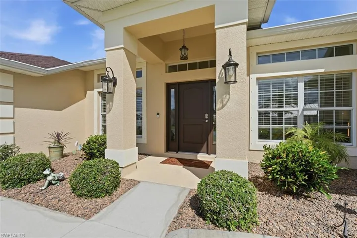 Stucco exterior featuring an inviting covered entryway, dark wood-finish entry door with sidelights, and exterior lighting fixtures