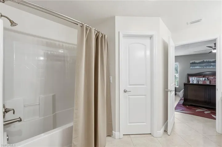 White tile flooring extends through this interior hallway, featuring a white paneled door with brushed nickel hardware and an adjacent bathroom with a white tub/shower combination