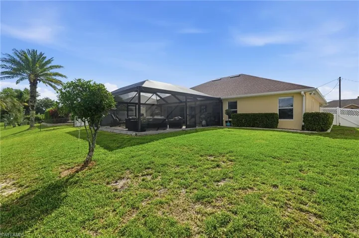 Expansive green lawn with a screened-in patio, mature palm trees, and established shrubs