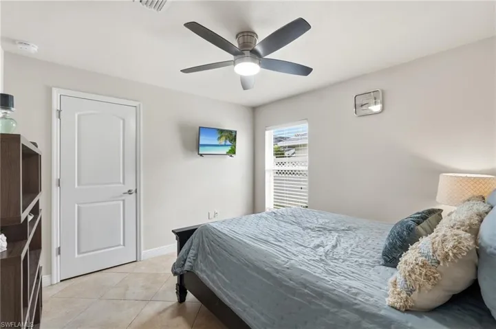 Bedroom featuring tile flooring, a window with horizontal blinds, a ceiling fan with integrated lighting, a paneled door, and neutral wall tones