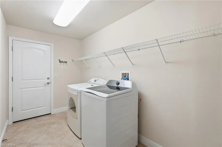 Laundry room featuring tile flooring, white wire shelving, a ceiling-mounted fluorescent light fixture, and a white paneled door