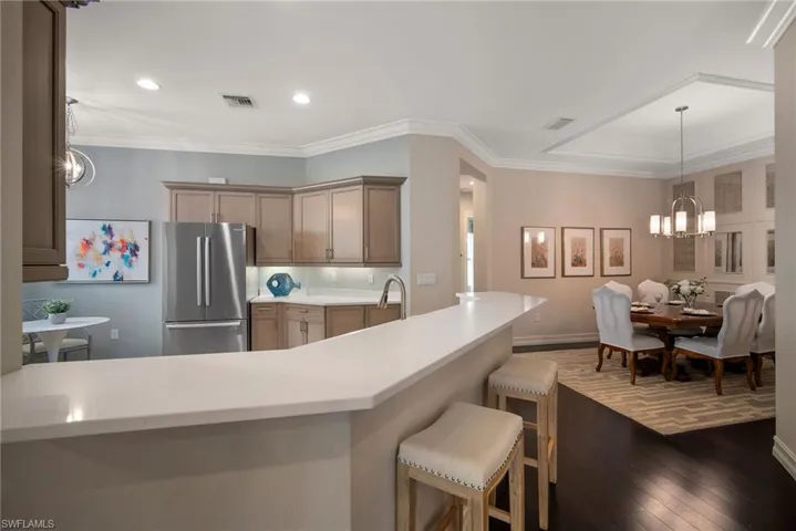 Kitchen featuring light tile floors, crown molding, hanging light fixtures, stainless steel fridge, and a notable chandelier