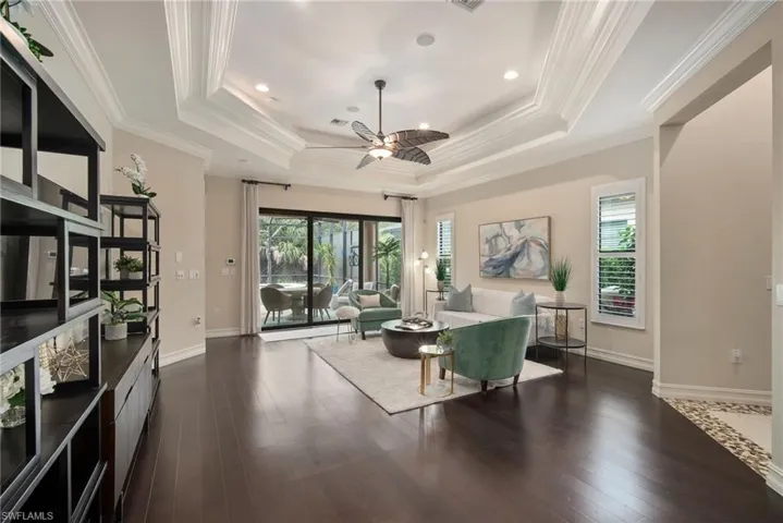 Living room featuring a tray ceiling, ornamental molding, dark hardwood / wood-style flooring, and ceiling fan