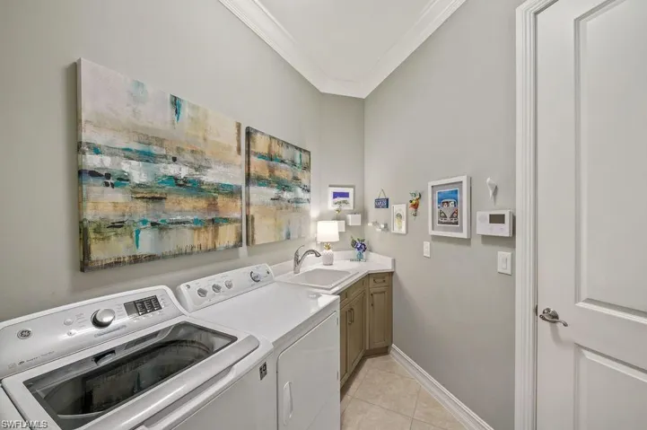 Laundry room with crown molding, cabinets, sink, light tile patterned flooring, and washing machine and dryer