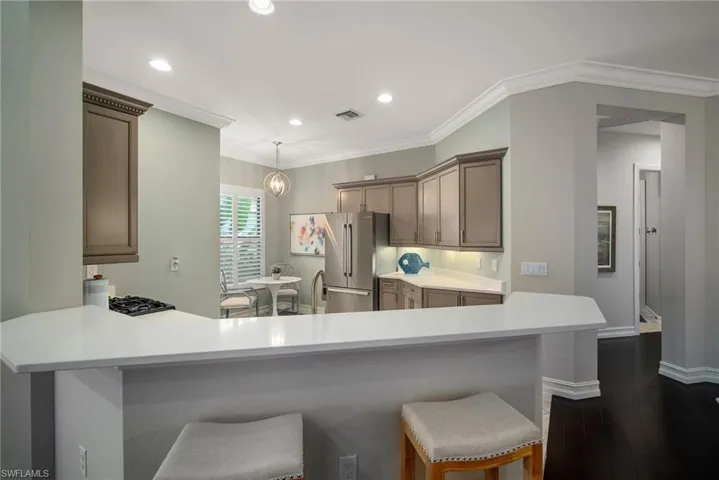 Kitchen featuring hanging light fixtures, light tile floors, a breakfast bar area, kitchen peninsula, and stainless steel refrigerator