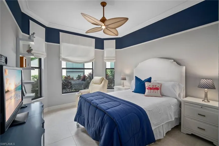 Tiled guest bedroom with ceiling fan, multiple windows, and crown molding