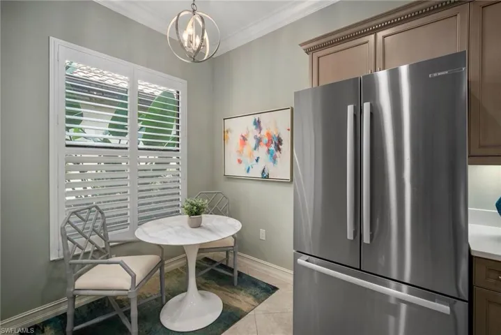 Kitchen featuring pendant lighting, an inviting chandelier, stainless steel refrigerator, ornamental molding, and light tile patterned floors