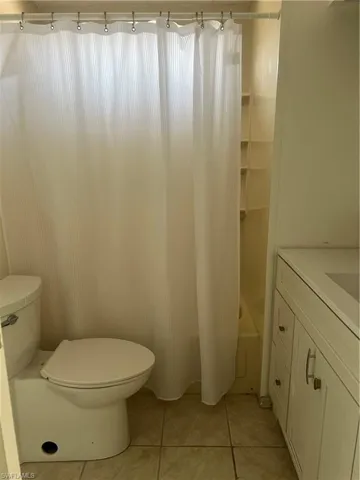 Bathroom with shower / tub combo with curtain, vanity, tile patterned flooring, and toilet