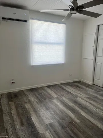 Empty room featuring baseboards, a ceiling fan, wood finished floors, and a wall mounted AC