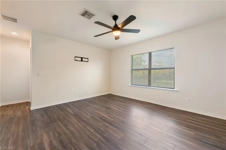 Spacious room featuring wood-finish flooring, a ceiling fan with integrated lighting, and a large window with blinds