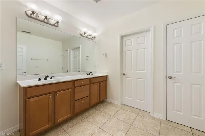 Dual sink vanity with wood-finish cabinetry, white countertop, and expansive mirror