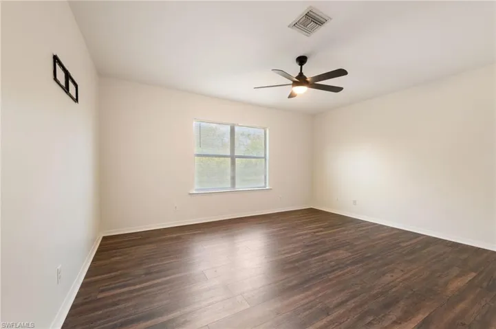 Spacious room featuring wood-finish flooring, a ceiling fan with integrated lighting, and a large window