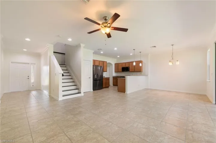 Spacious main living area featuring tile flooring, a functional kitchen with wood-finish cabinetry, a central ceiling fan, a prominent staircase, and recessed lighting