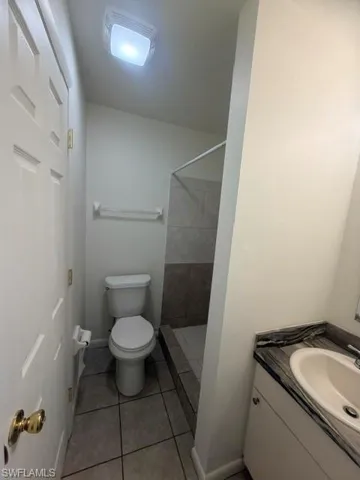 Bathroom featuring a single vanity with an integrated sink and dark stone-look countertop, a standard toilet, and a tiled shower stall