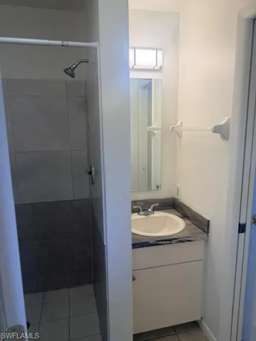 Bathroom featuring a white vanity with an undermount sink, granite-finish countertop, and a tiled shower enclosure