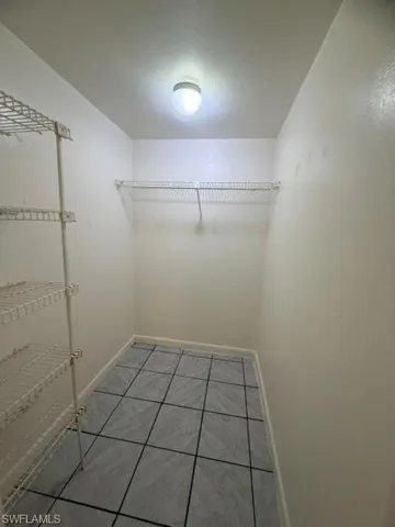 Utility space featuring a surface-mounted ceiling light, white wire shelving, a single wire hanging rod, and gray square floor tiles
