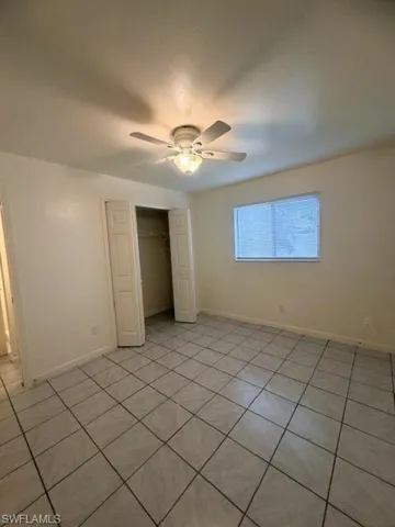 Spacious room with light-toned tiled flooring, a ceiling fan with integrated lighting, a window with horizontal blinds, and a double-door closet with shelving