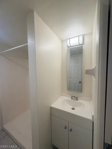 Compact bathroom featuring a white vanity with integrated sink, rectangular mirror, and an overhead vanity light