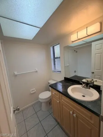 Bathroom featuring a light wood-finish vanity with a dark countertop and an integrated sink, a large mirror, a privacy window, and tiled flooring
