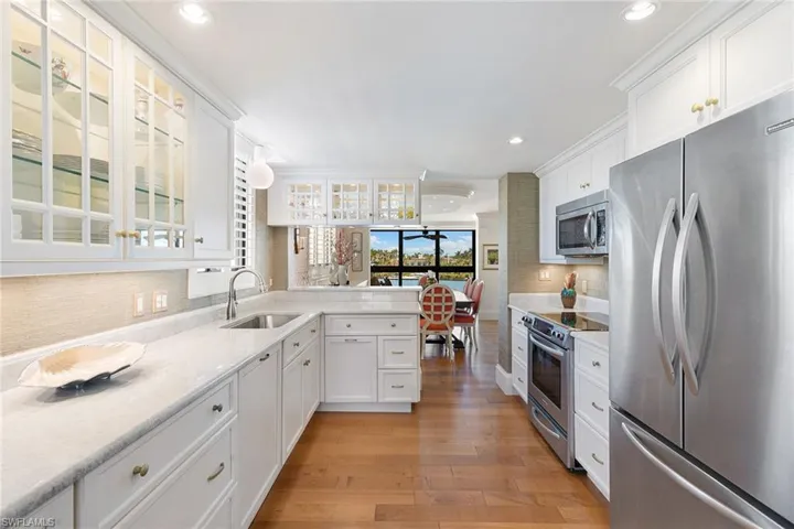 Kitchen with appliances with stainless steel finishes, white cabinetry, light stone counters, backsplash, and light wood finished floors