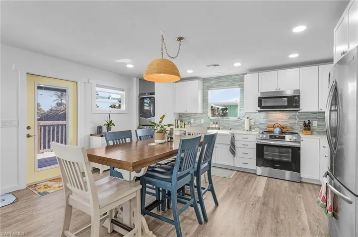 Kitchen with white cabinets, hanging light fixtures, stacked washer / dryer, and stainless steel appliances.  Also, second door that leads to the back wood deck.