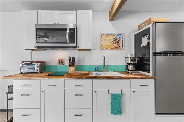Kitchen with butcher block countertops, white cabinetry, sink, and stainless steel appliances.