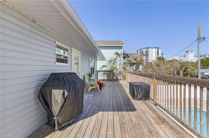 Rear of the home off of the wooden deck with a grill a great elevation view of the pool.