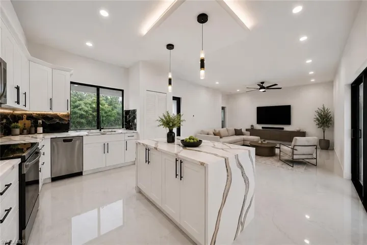 Open-concept kitchen and living area featuring a waterfall-edge island, white cabinetry with black hardware, recessed lighting, and stainless steel appliances