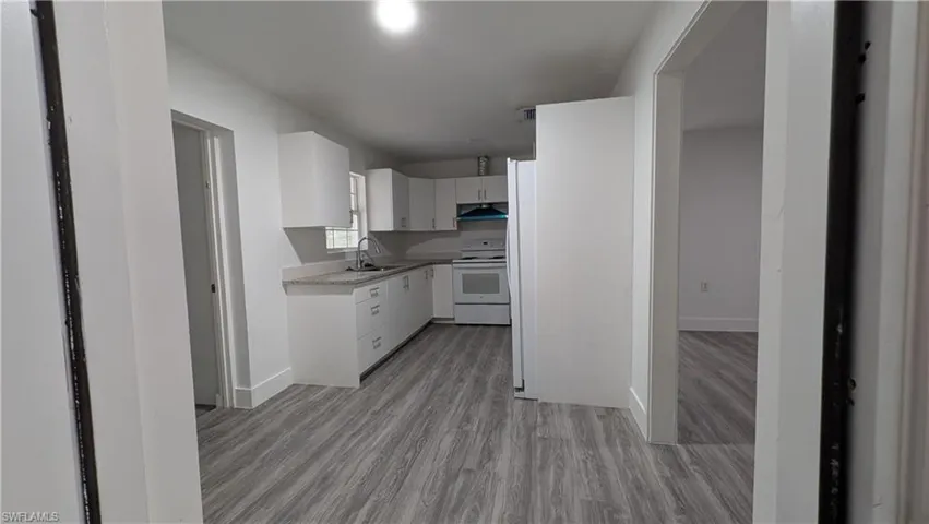 Kitchen featuring white cabinets, light countertops, white appliances, and light wood-style flooring