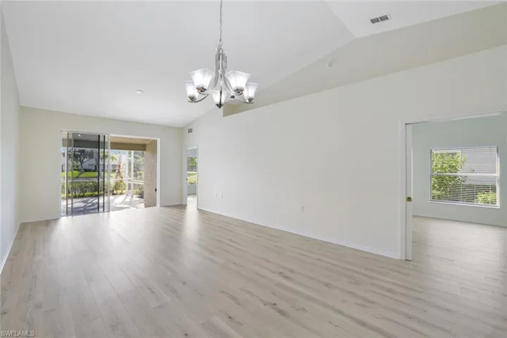 Empty room with vaulted ceiling, a chandelier, and light wood finished floors