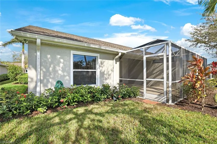 View of side of home with a lawn, stucco siding, glass enclosure, and roof with shingles