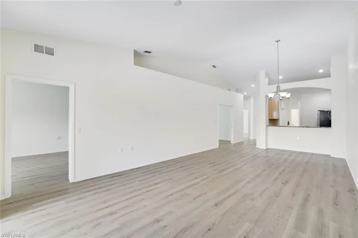 Unfurnished living room featuring a chandelier, light wood-style floors, arched walkways, and high vaulted ceiling