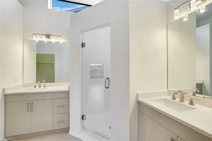 Bathroom featuring a shower stall, two vanities, and a walk in closet