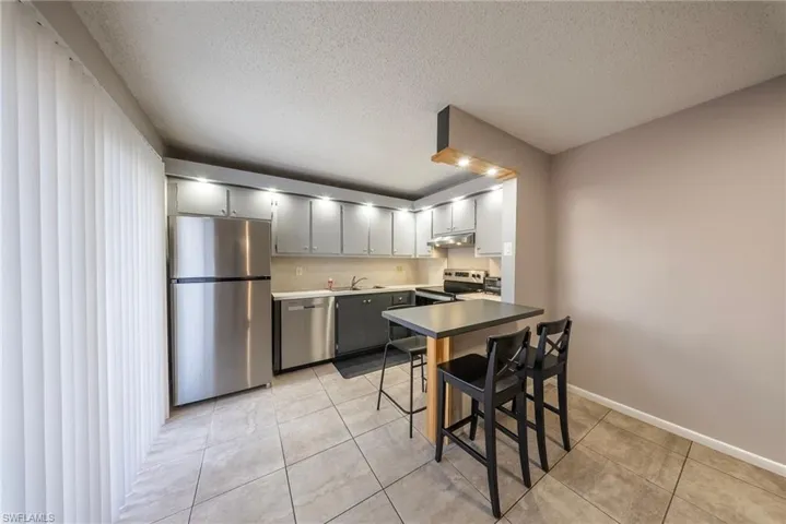 Kitchen featuring stainless steel appliances, a breakfast bar area, a textured ceiling, light tile patterned floors, and a peninsula