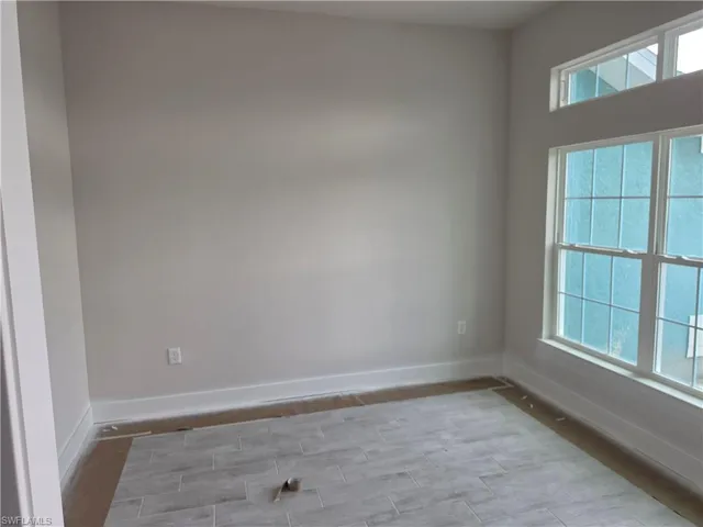 Bright interior space featuring a multi-pane window, transom window, light gray wall finish, white baseboards, and wood-finish tile flooring