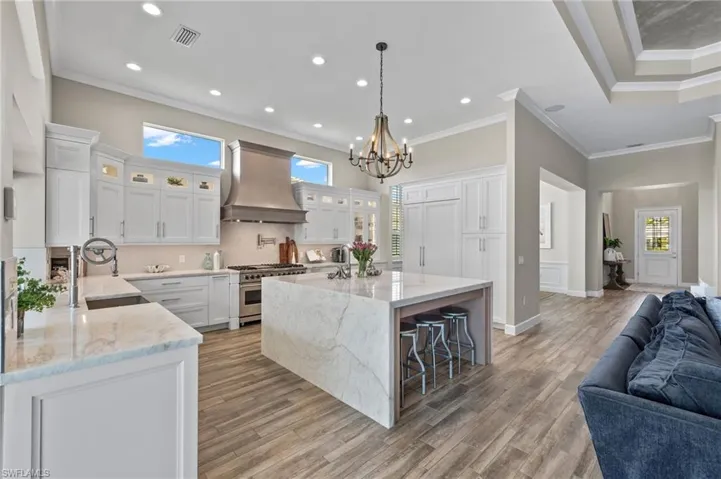 Kitchen featuring custom range hood, crown molding, a center island with sink, and range with two ovens