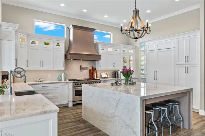Kitchen with high end stainless steel range, a kitchen island, custom range hood, light stone counters, and backsplash