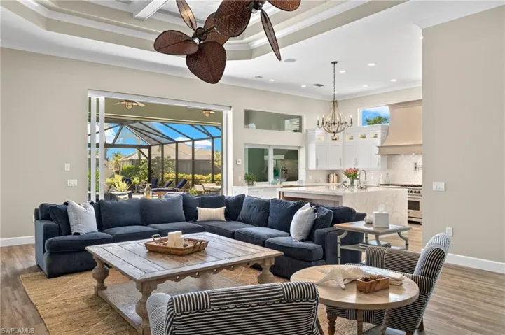 Living room with hardwood / wood-style floors, a raised ceiling, ceiling fan with notable chandelier, sink, and ornamental molding