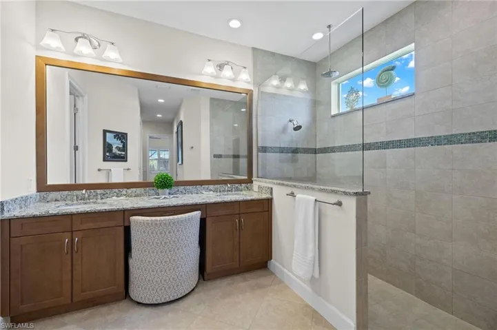 Bathroom featuring tiled shower, tile floors, double sink, and vanity with extensive cabinet space