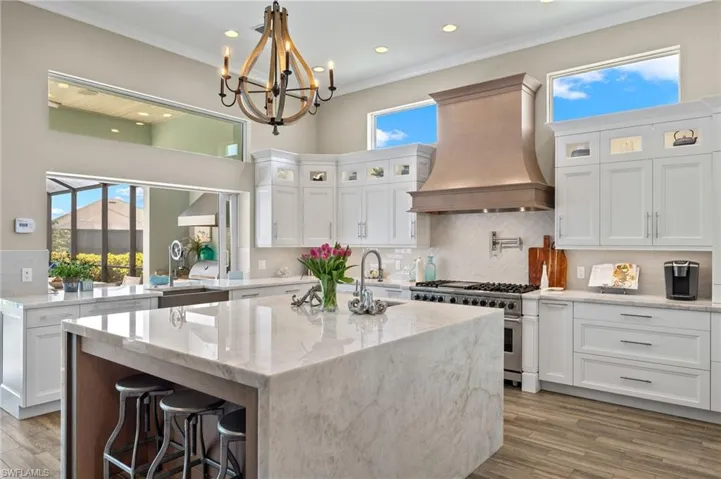 Kitchen featuring hardwood / wood-style floors, tasteful backsplash, custom exhaust hood, a center island with sink, and range with two ovens
