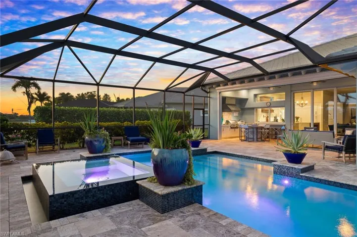 Pool at dusk with a patio area, glass enclosure, an in ground hot tub, and an outdoor bar