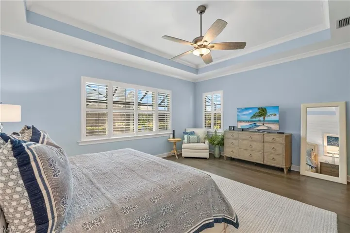 Bedroom with ceiling fan, ornamental molding, a tray ceiling, and dark hardwood / wood-style floors