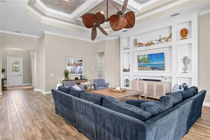 Living room with coffered ceiling, ceiling fan, ornamental molding, and light hardwood / wood-style floors
