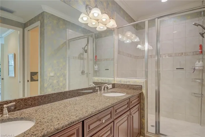 Bathroom featuring crown molding, double vanity, a shower stall, wallpapered walls, and a chandelier