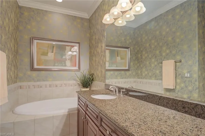 Bathroom with wallpapered walls, ornamental molding, a bath, vanity, and a chandelier